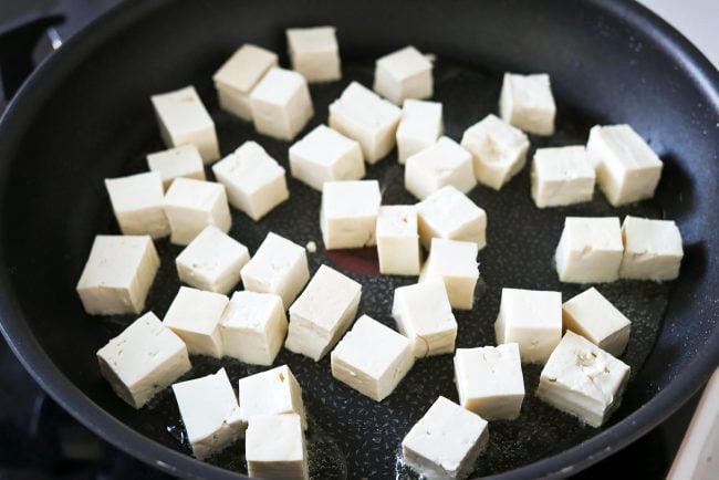 White tofu cubes in a black nonstick skillet with a bit of oil.