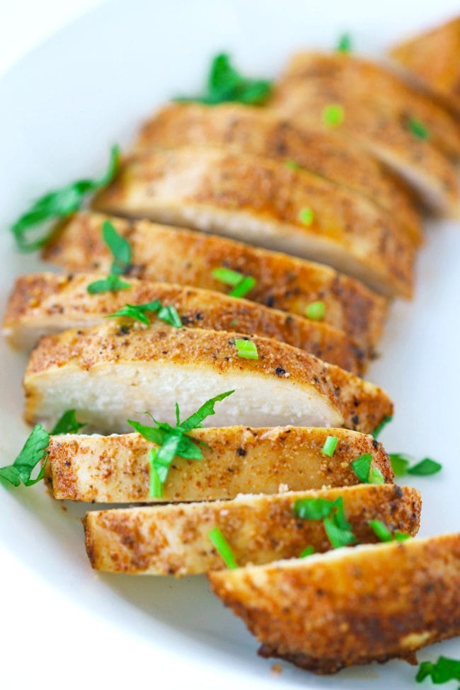 Close up of a seasoned and baked sliced chicken breast that's fanned out in a white round plate and garnished with fresh chopped parsley.