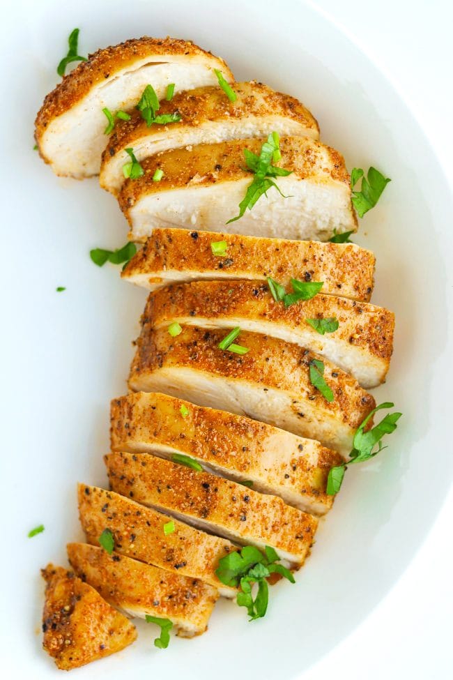 A sliced seasoned baked chicken breast in a white plate garnished with  chopped parsley.
