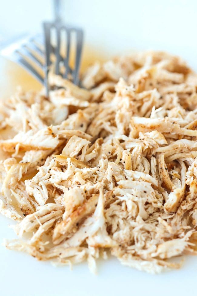 Shredded chicken on a chopping board with two silver forks.