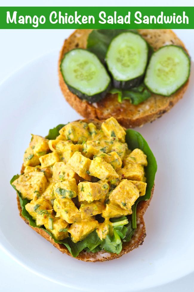 10 cereal bagel halves on a plate with spinach leaves, cucumber slices, and mango chicken salad.