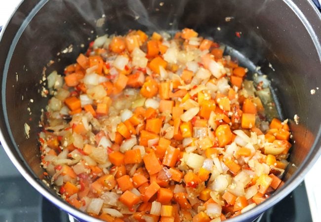 Deglazing pot on stovetop with sautéed diced carrots, onion, garlic, and chopped red chilies with dry white wine.