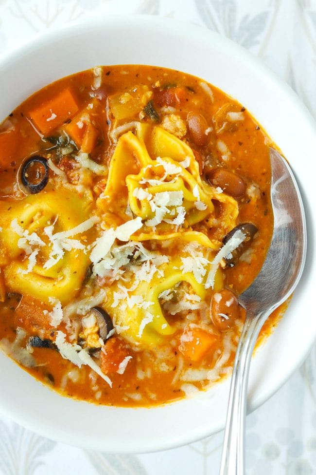Close up of tomato basil tortellini soup is a white bowl with a spoon.