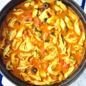 Creamy tomato basil tortellini soup in a blue Dutch oven on top of a floral grey napkin.