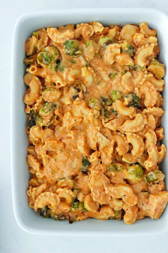 Large white long baking dish with harissa mac and cheese with chicken and brussels sprouts.