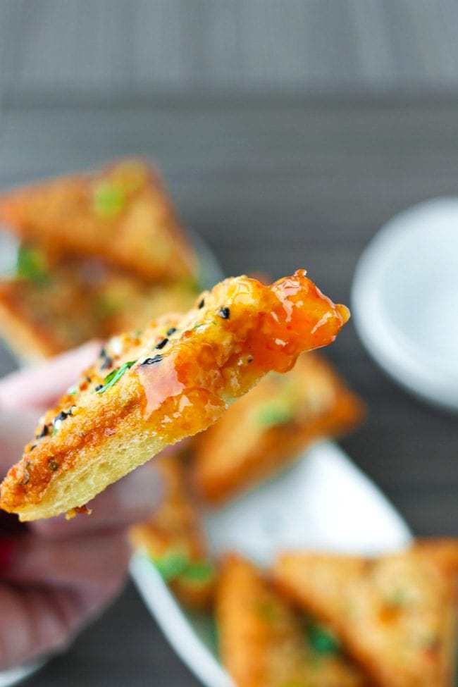 Hand holding up a prawn toast piece dipped in Thai Sweet Chili Sauce.