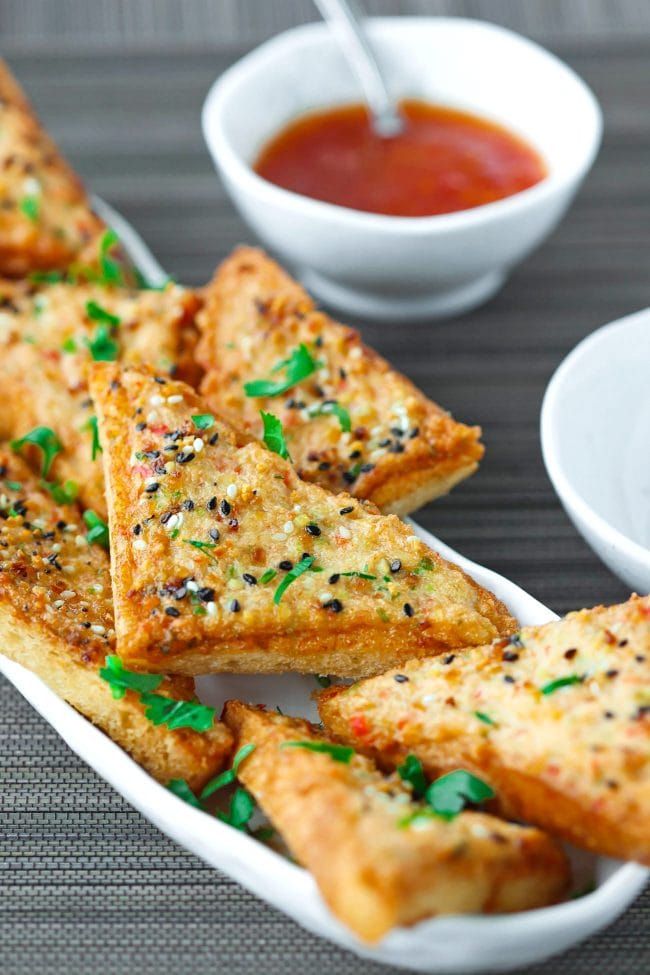 Prawn Toast triangles on a long plate garnished with chopped coriander and served with a small bowl of Thai Sweet Chili Sauce on the side.