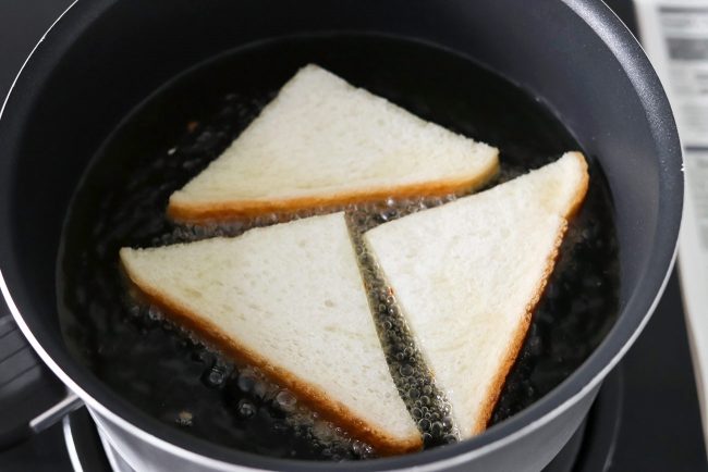 Three bread triangles frying in a pot of bubbling oil on the stovetop.