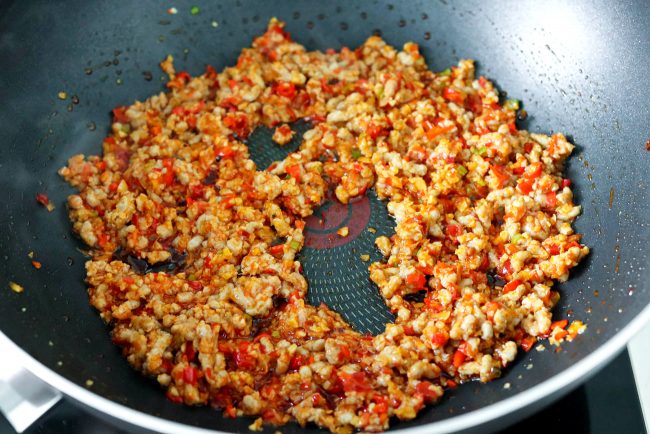 Ground pork being cooked and tossed with chili bean paste and aromatics in a black wok on the stovetop.