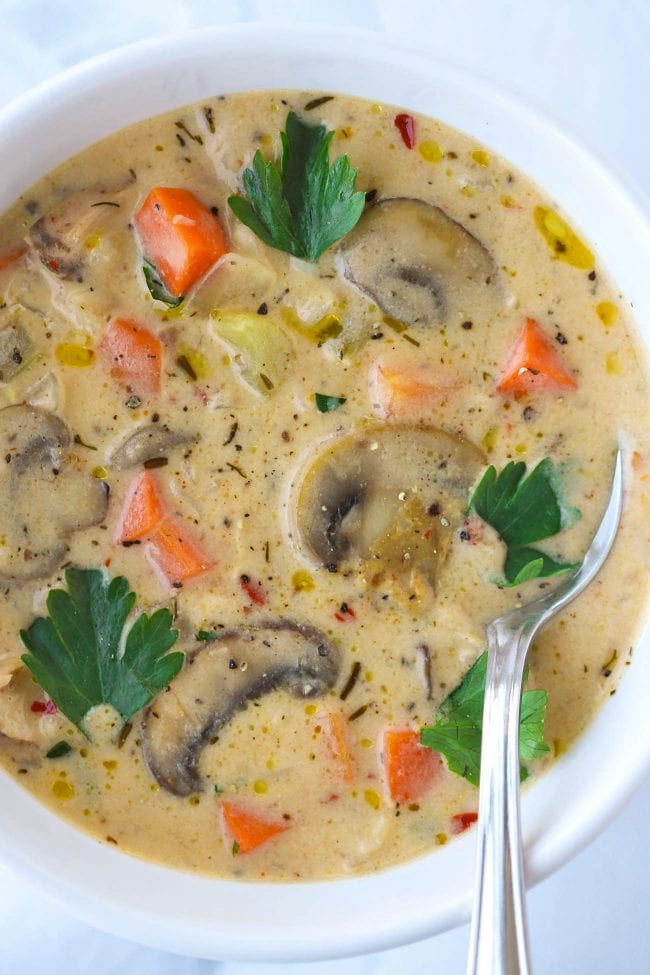White round bowl with creamy mushroom and chicken vegetable soup and a spoon.
