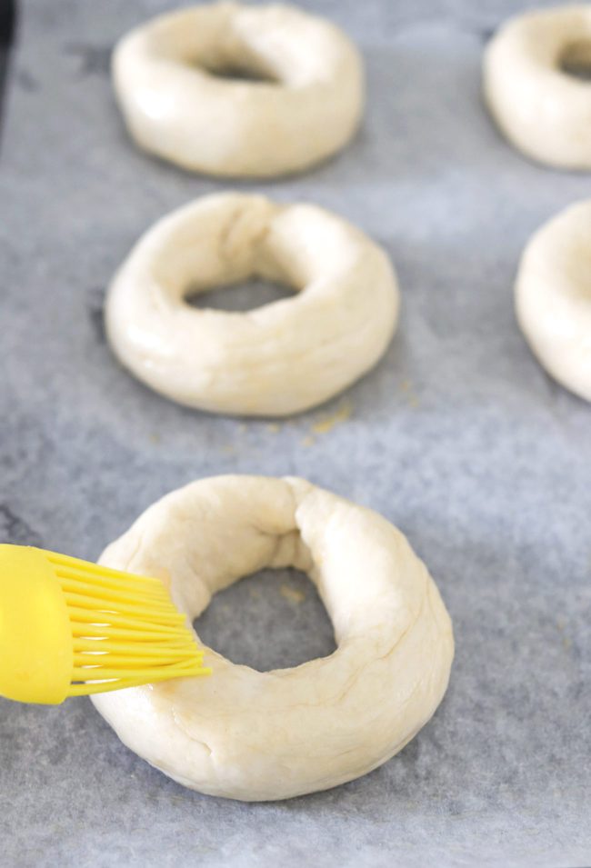 Brushing egg wash on bagel rings on a parchment paper lined baking tray.