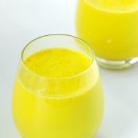 Two drink glasses with yellow turmeric milk and spices.