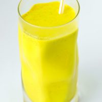 Yellow turmeric milk with spices in a tall fancy glass with a straw.