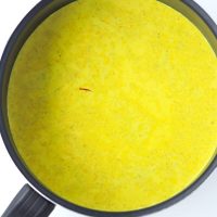 Yellow turmeric milk with spices in a black saucepan.