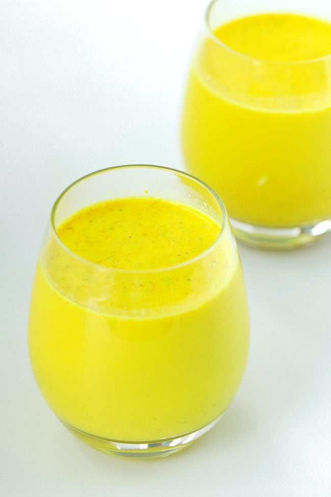 Yellow turmeric milk with spices in a two small drink glasses.