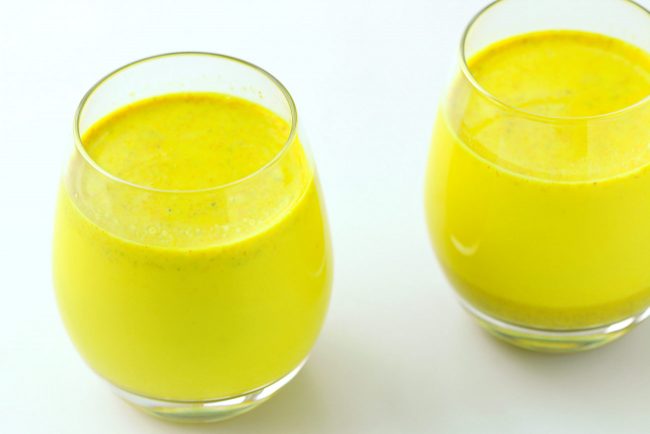 Two drink glasses with yellow turmeric milk with spices.