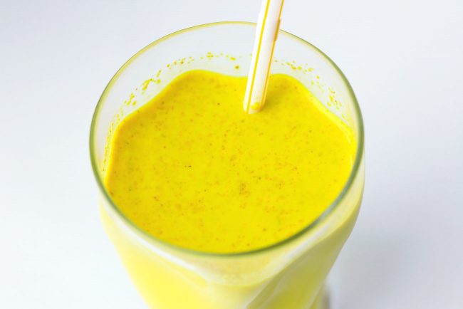 Top view of tall glass with yellow turmeric milk with spices.