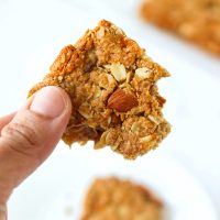 Hand holding up an apricot and almond oat slice with a bite taken out of it.