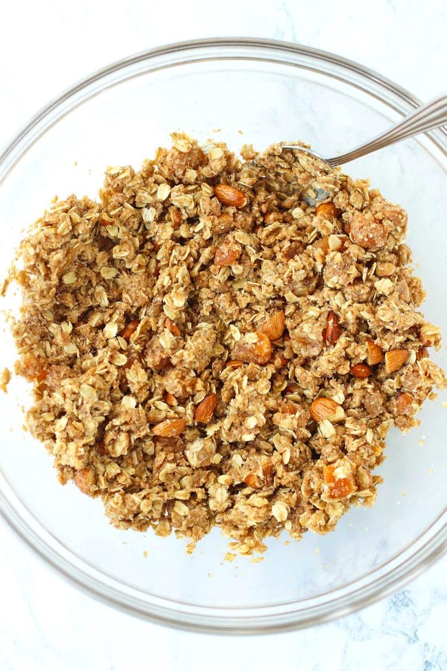 Wholegrain wheat flour, desiccated coconuts, old fashioned rolled oats, light brown sugar, chopped almonds, chopped dried apricots, and baking soda mixed together with a spoon in a large mixing bowl.
