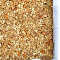 Unbaked apricot almond oat slice mixture in a parchment paper lined baking pan.