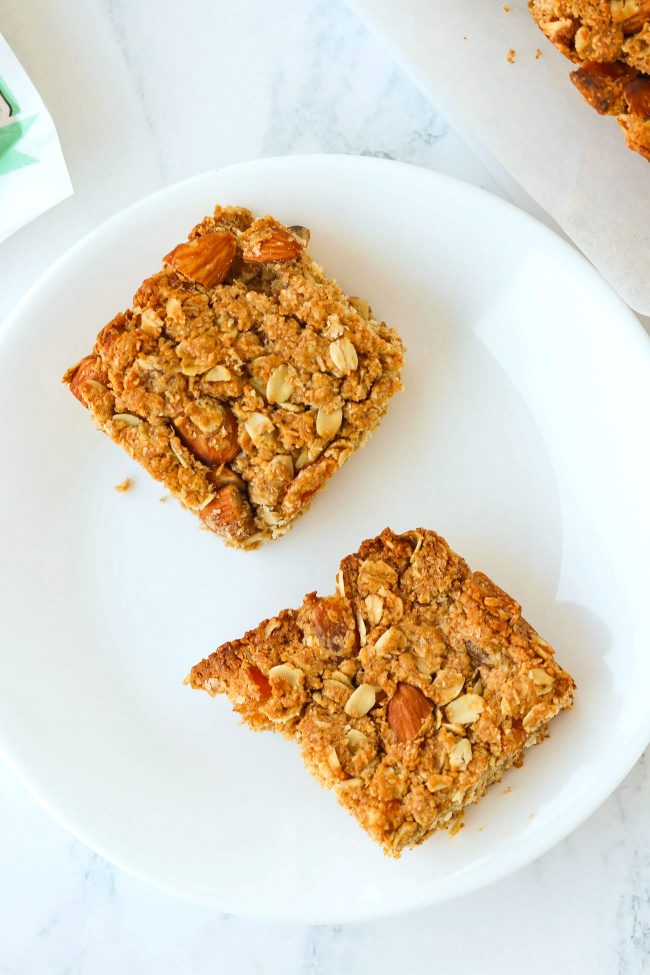 Two apricot and almond oat slices on a white round plate.