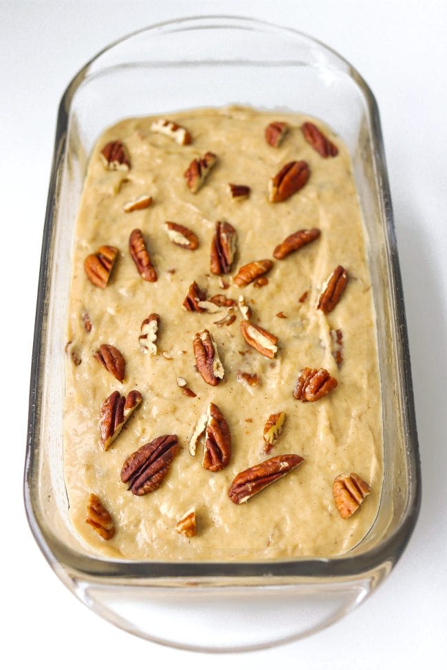 Batter topped with chopped pecans in a glass loaf dish.