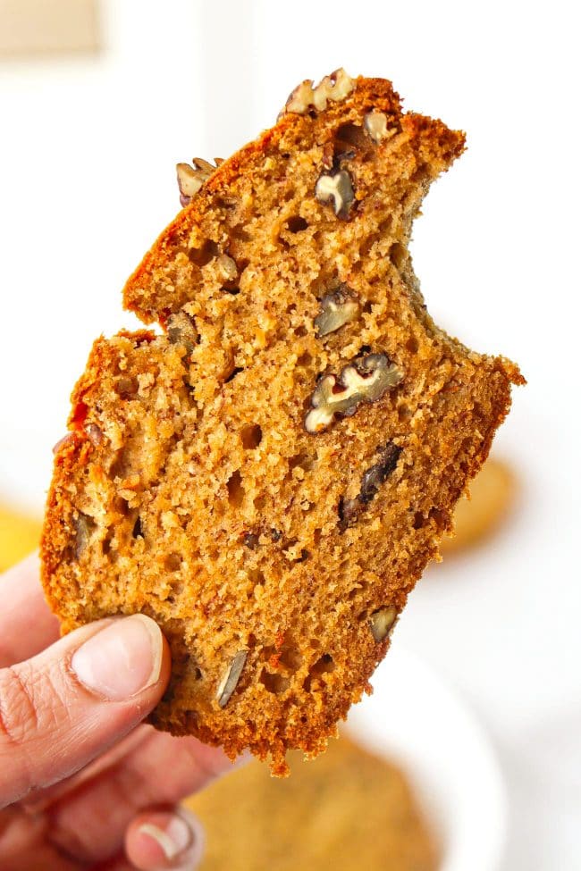 Hand holding up a slice of Banana Pecan Bread with a bite taken out of it.