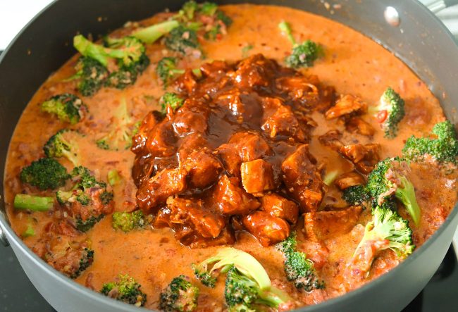 BBQ sauce diced chicken pieces in a pan with creamy spicy tomato sauce and broccoli florets.