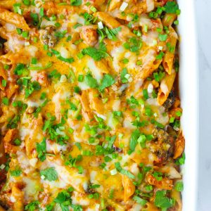 Large baking dish with Spicy BBQ Chicken Penne Pasta with corn, broccoli, melted cheese, and garnished with chopped coriander and spring onion.