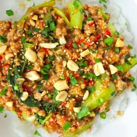 Ground pork and bok choy peanut sauce stir-fry on rice in plate and topped with sesame seeds, chopped peanuts, coriander, and spring onion. Serving bowl with the stir-fry and bowl with peanuts in the back.
