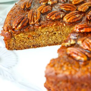 Almond Meal Banana Cake with honey pecan glaze on a large round plate with a slice cut out to show the inside texture.