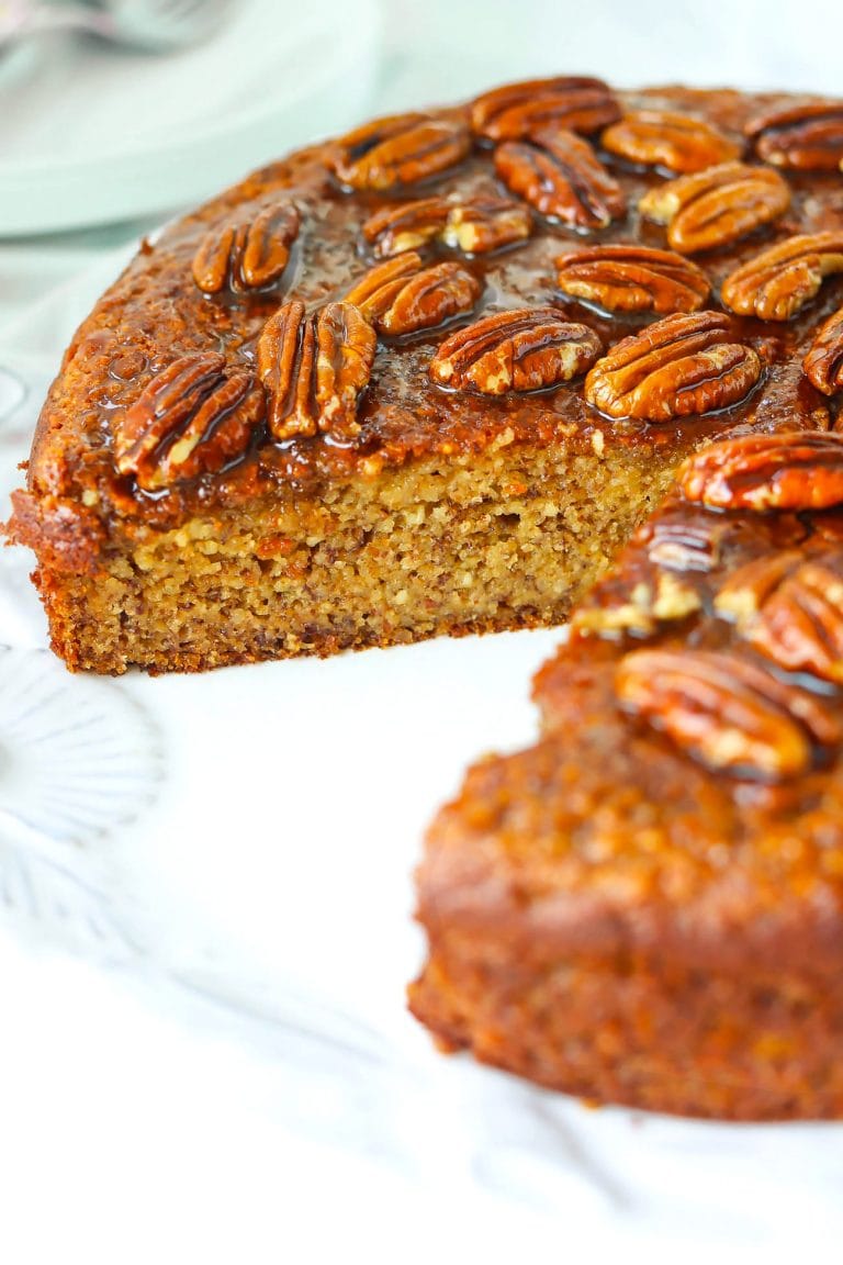 Almond Meal Banana Cake with honey pecan glaze on a large round plate with a slice cut out to show the inside texture.