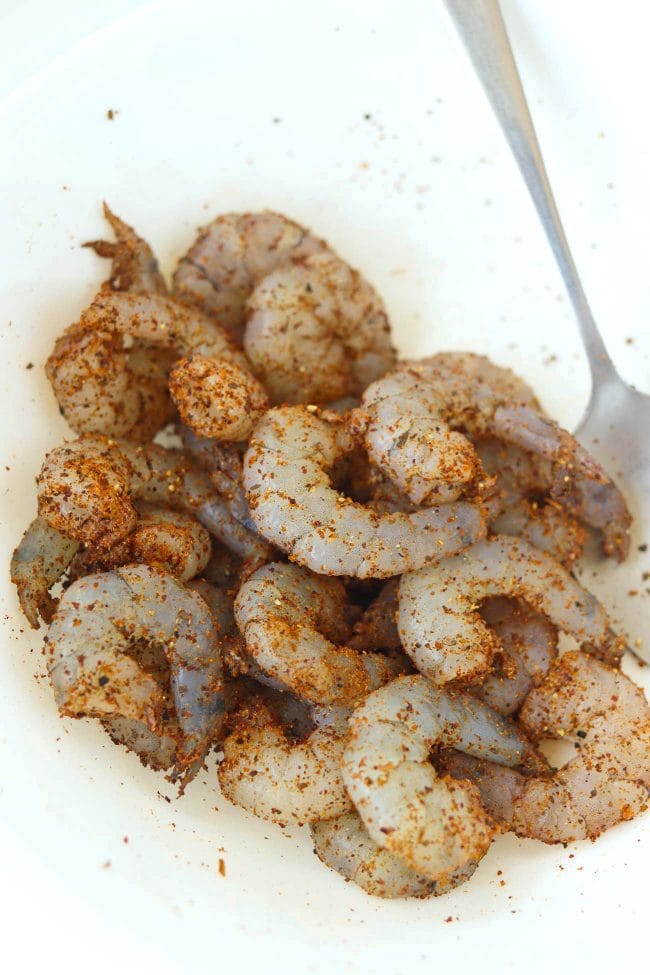 Shrimp coated with seasonings in a bowl with a spoon.