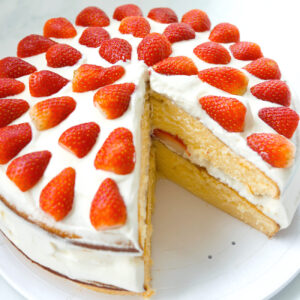 Top front angle view of strawberry lemon cream layer cake on a platter with a slice cut out to show inside of cake.