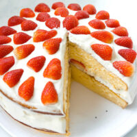 Overhead front view of layer cake on a platter with a slice cut out to show inside of cake. Text overlay "Strawberry Lemon Cream Cake".