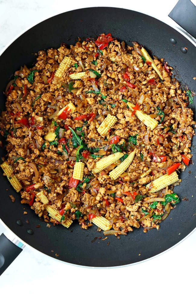 Thai holy basil chicken stir-fry with baby corn in a large wok.