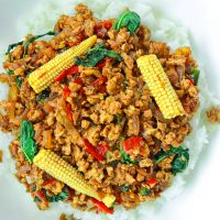 Top view of plate with rice topped with ground chicken Thai basil stir-fry with sliced baby corn.