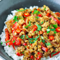 Ground pork stir-fry with onion, chilies, red bell pepper, mint, and coriander in a black bowl with rice.