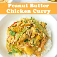 Front view of plate with rice topped with Peanut Butter Chicken Curry and garnished with chopped coriander and peanuts. Serving bowl with curry and bowl with chopped peanuts in the back. Text overlay "Peanut Butter Chicken Curry".