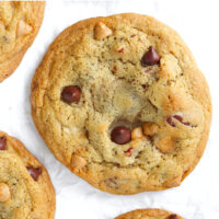 Close up of a chocolate butterscotch chip pecan cookie surrounded by other cookies on crinkled parchment paper. Text overlay "Soft & Chewy Chocolate Butterscotch Chip Pecan Cookies".