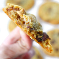 Close up of a hand holding up a chocolate butterscotch chip pecan cookie with a few bites taken out of it. Text overlay "Soft & Chewy Chocolate Butterscotch Chip Pecan Cookies".