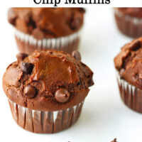 Close up of muffins lined up on parchment paper with chocolate chips scattered in front. Text overlay "Double Chocolate Chip Muffins*.