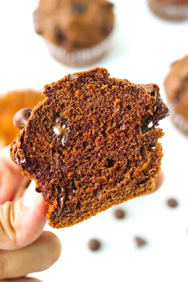 Hand holding up half a muffin to show inside with melty chocolate chips.