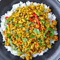 Close up top view of ground pork stir-fry on rice in black bowl. Text overlay "Khua Kling Moo (Southern Thai Dry Curry Pork)".