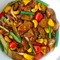 Top view of stir-fry chicken dish with bell peppers and cashews in a round serving bowl.
