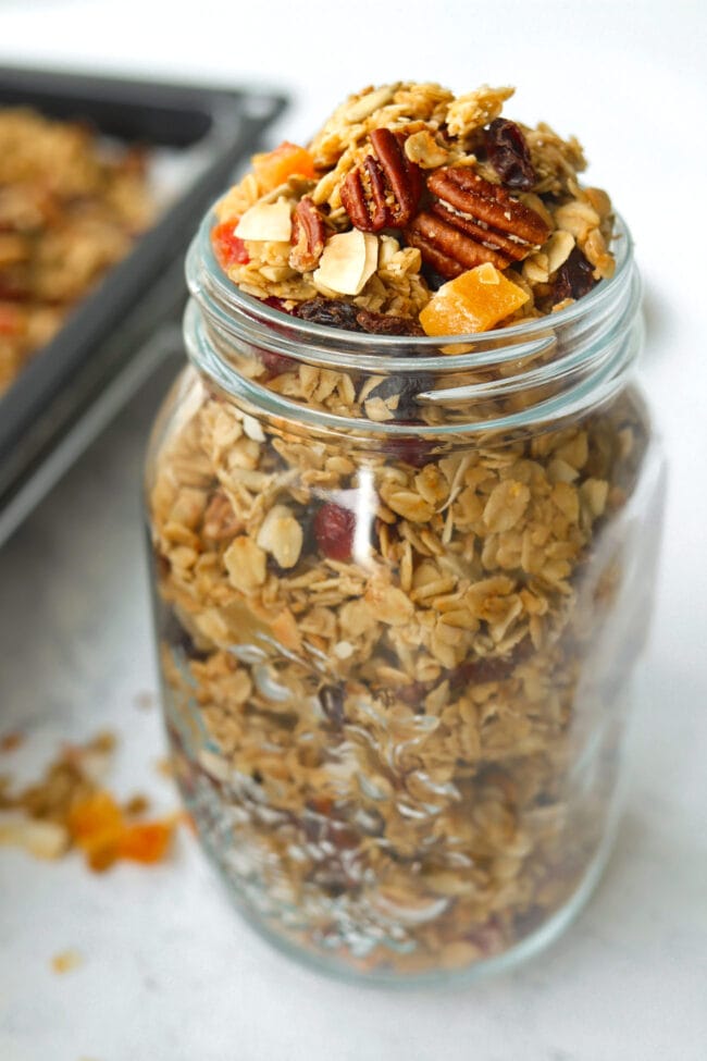 Front view of overfilled mason jar with granola, and scattered clusters around jar.