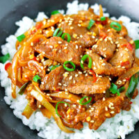 Close-up front view of bowl with spicy pork stir-fry on rice. Text overlay "Spicy Korean Pork Stir-fry".