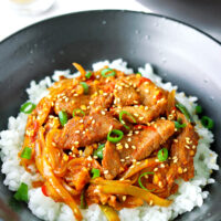 Front view of bowl with spicy pork stir-fry on rice. Text overlay "Spicy Korean Pork Stir-fry".