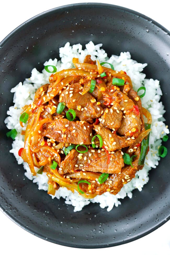 Close up top view of black bowl with spicy pork stir-fry on rice.