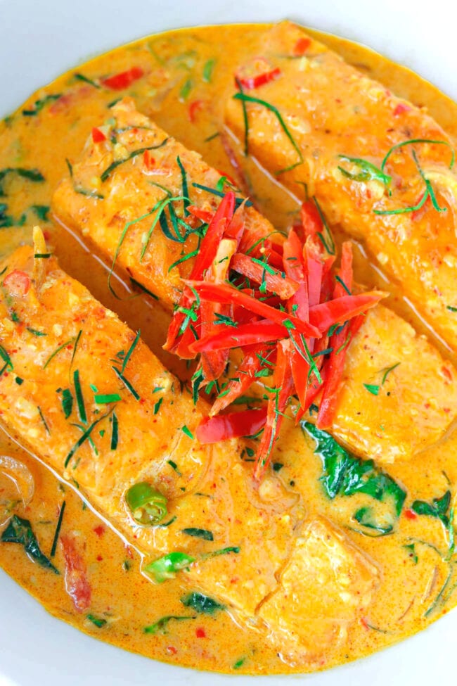 Top close-up view of salmon fillets in Thai red curry sauce in a bowl.